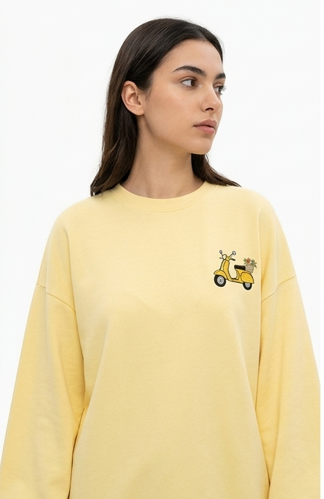 A woman modeling a pale yellow long-sleeve sweatshirt in three views: front, side, and back. The front shows a small yellow graphic on the left chest, while the back features a large collage print with multiple small images and text.